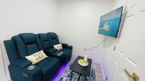 Ein Wohnzimmer mit einem türkisfarbenen Sofagarnitur, einem kleinen Tisch mit einer Kerze und einem an der Wand befestigten Fernseher.