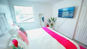 Quarto com cama, janela, televisão na parede e porta.