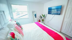 Une chambre à coucher avec un lit, une fenêtre, un téléviseur fixé au mur et une porte.