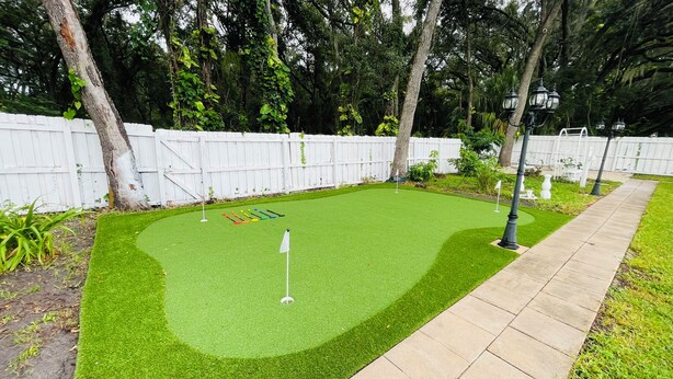 Um campo de mini golfe com cerca branca, grama sintética verde e um caminho.