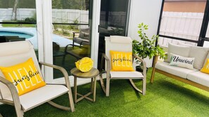 Une pièce avec une piscine, deux fauteuils avec des coussins, une petite table et un canapé avec des oreillers.