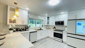 Cozinha moderna com armários brancos, forno embutido, micro-ondas e espaço para café.