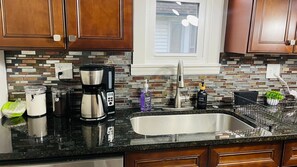 A kitchen with wooden cabinets, a black countertop, a stainless steel sink, a coffee maker, and a window above the sink. - The West Blvd 2bedroom Central close to HWY (Cleveland)