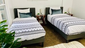 A double room with two beds, each with patterned bedding and pillows, a small bedside table with a lamp, and a plant on one side. - The West Blvd 2bedroom Central close to HWY (Cleveland)