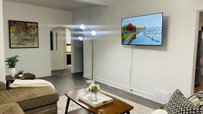 A modern living room with a flat-screen TV mounted on the wall, a coffee table with a vase of flowers, and a sofa. - The West Blvd 2bedroom Central close to HWY (Cleveland)