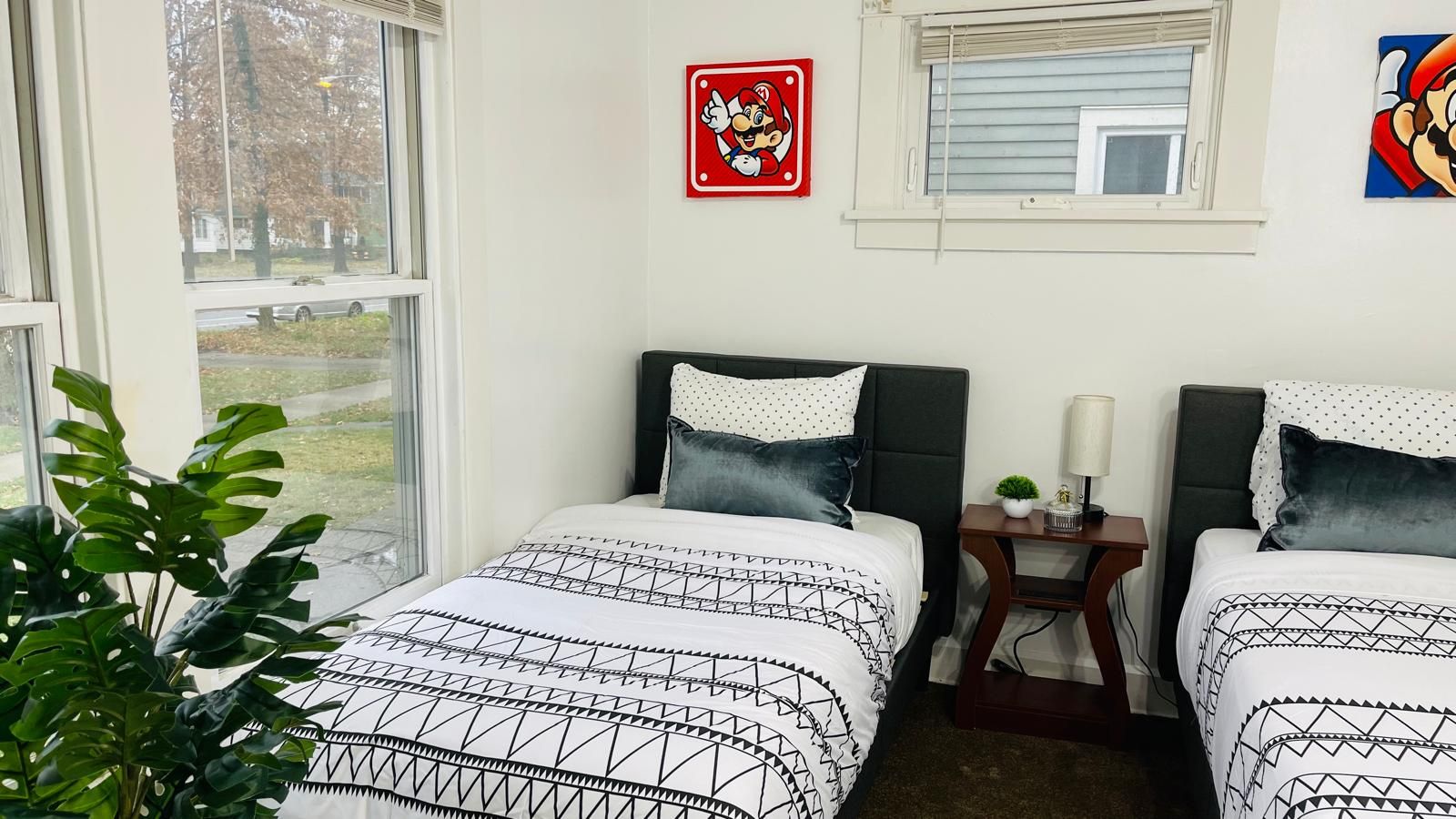 A bedroom with two beds, a window, a plant, and a Mario sign on the wall.