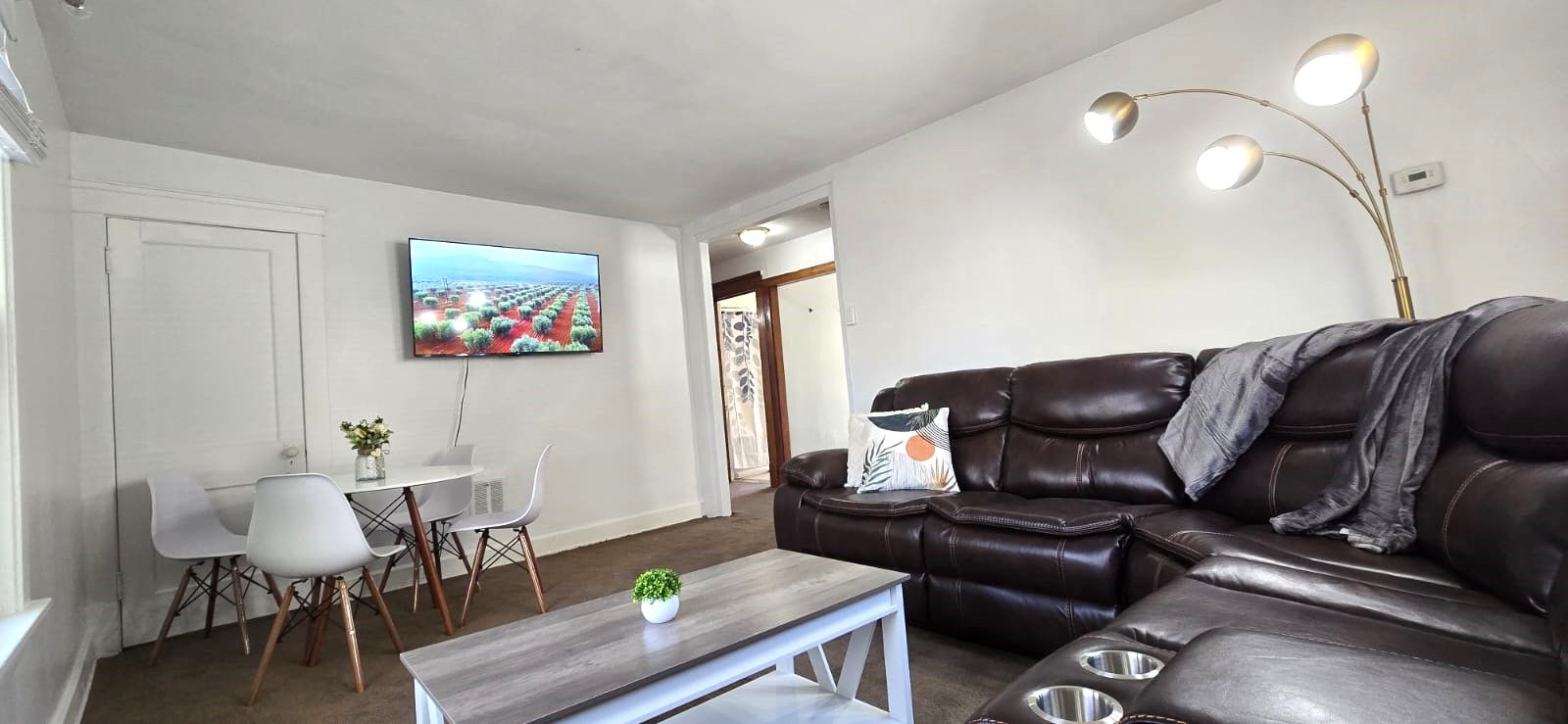 Un saló amb un sofà de cuir, una taula de centre, un televisor i una zona de menjador amb caires i una taula.