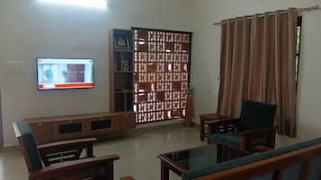 A living room with a television, wooden furniture, a decorative partition, and a curtain.
