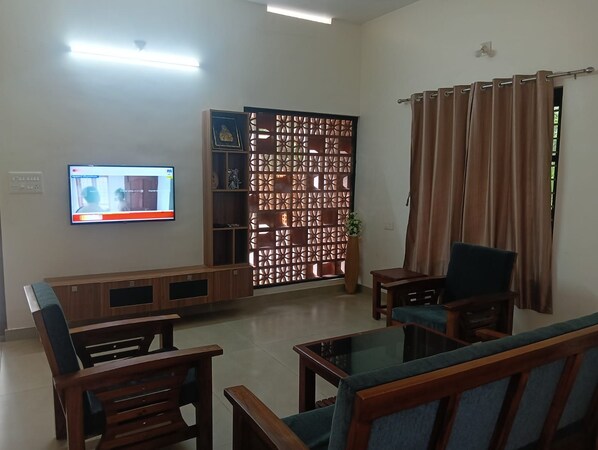 A living room with a television, wooden furniture, a decorative partition, and a curtain.