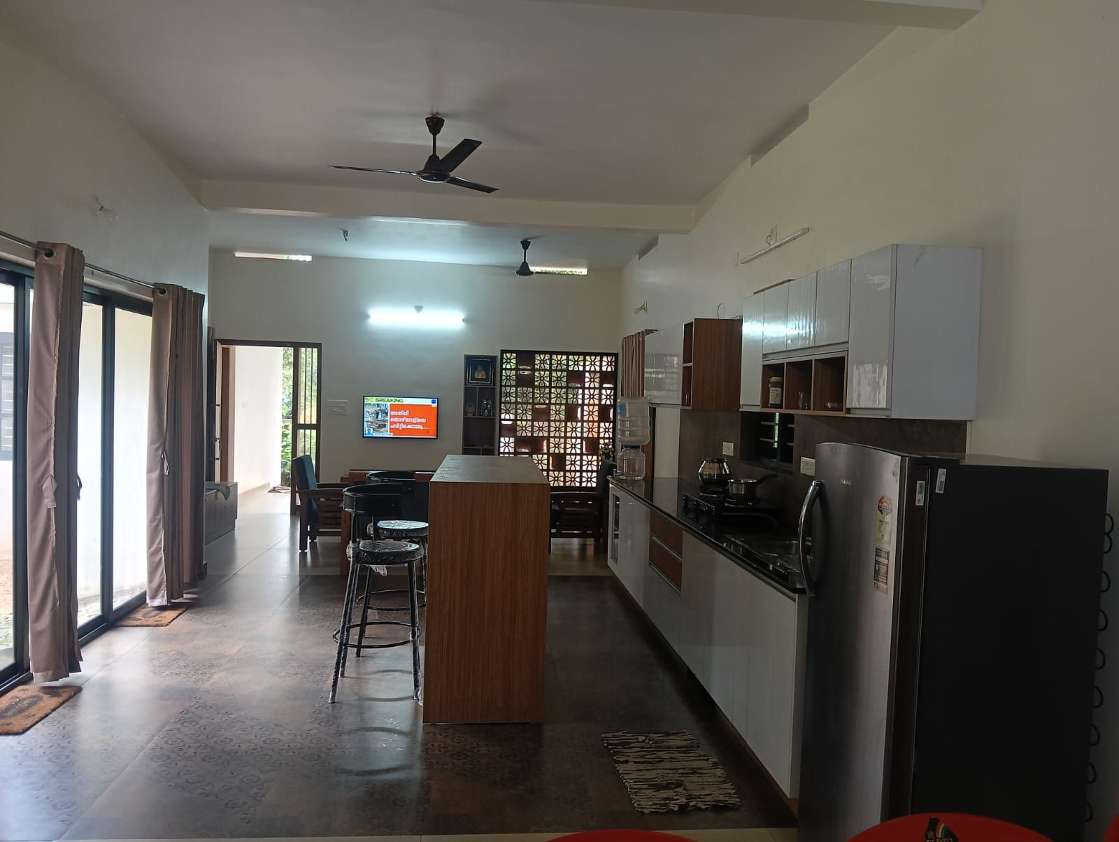A modern kitchen with a central island, a dining area with chairs, and a TV mounted on the wall.