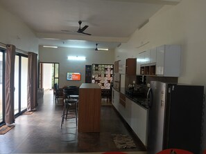 A modern kitchen with a central island, a dining area with chairs, and a TV mounted on the wall.