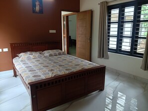 A bedroom with a wooden bed, a large window with blinds, and a door leading to another room.