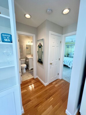 A hallway with wooden flooring, a white door, and a bathroom visible through an open door. - Seascape Retreat 2bd/2bth Balcony Waterview (Ocean City)
