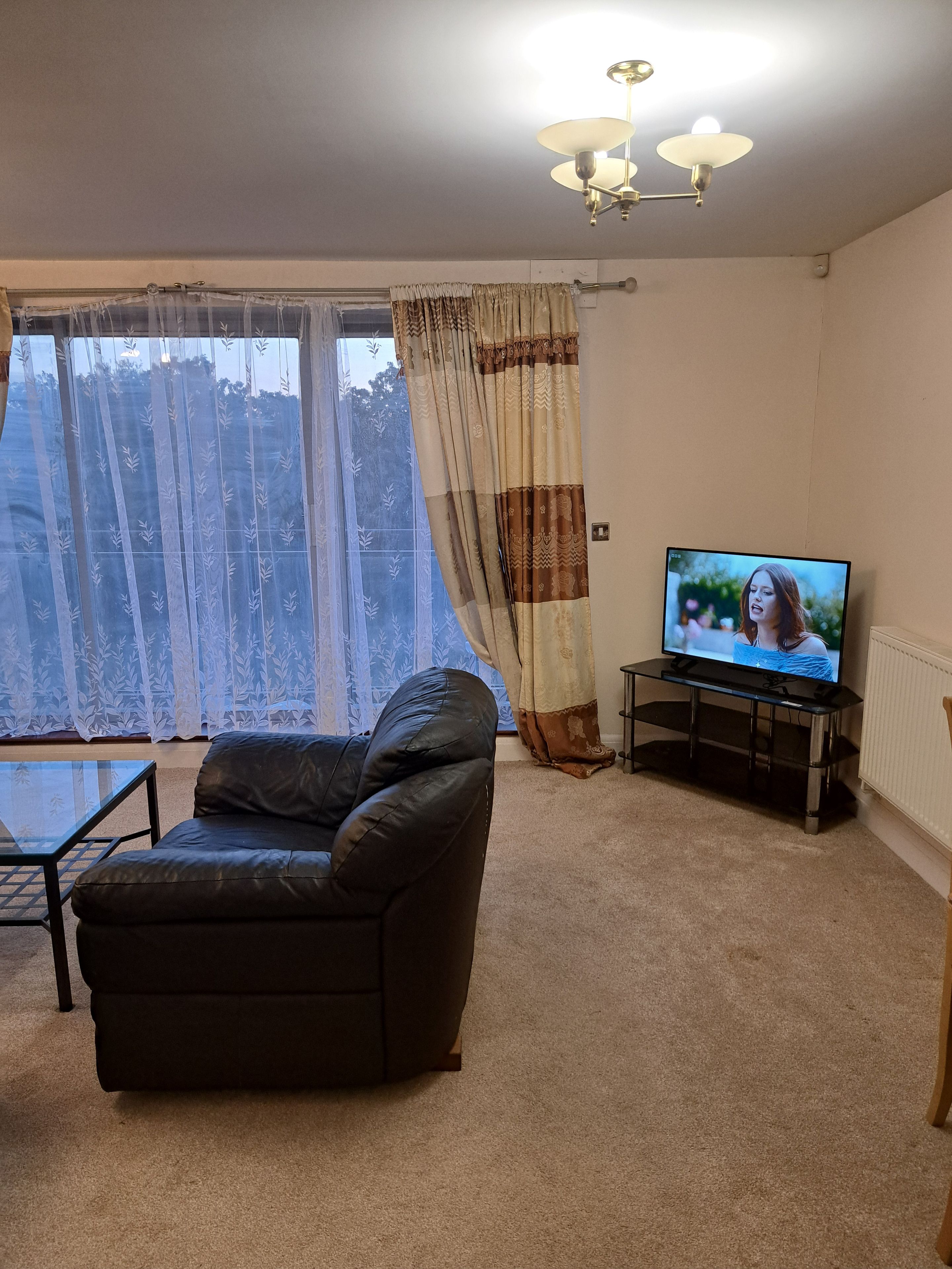 A living room with a leather sofa, a glass coffee table, a television on a stand, and a window with curtains.