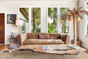 Una habitación con sofá de cuero, una mesa de centro con libros, una lámpara y un ventanal con vista a árboles.