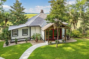 Ein kleines, eingeschossiges Haus mit Veranda, umgeben von einem gepflegten Rasen und Bäumen.