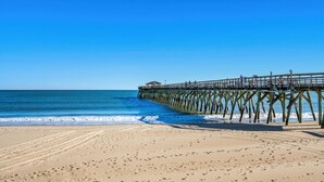Ein Strand mit einer hölzernen Seebrücke, die sich ins Meer erstreckt.