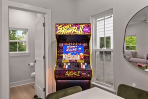Quarto com console de jogos, vaso sanitário, janela e espelho.