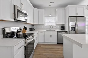 A modern kitchen with white cabinetry, a stainless steel refrigerator, a built-in oven, and a microwave. - Pop Art Paradise 2.5 Blocks Beach Pets (Myrtle Beach)