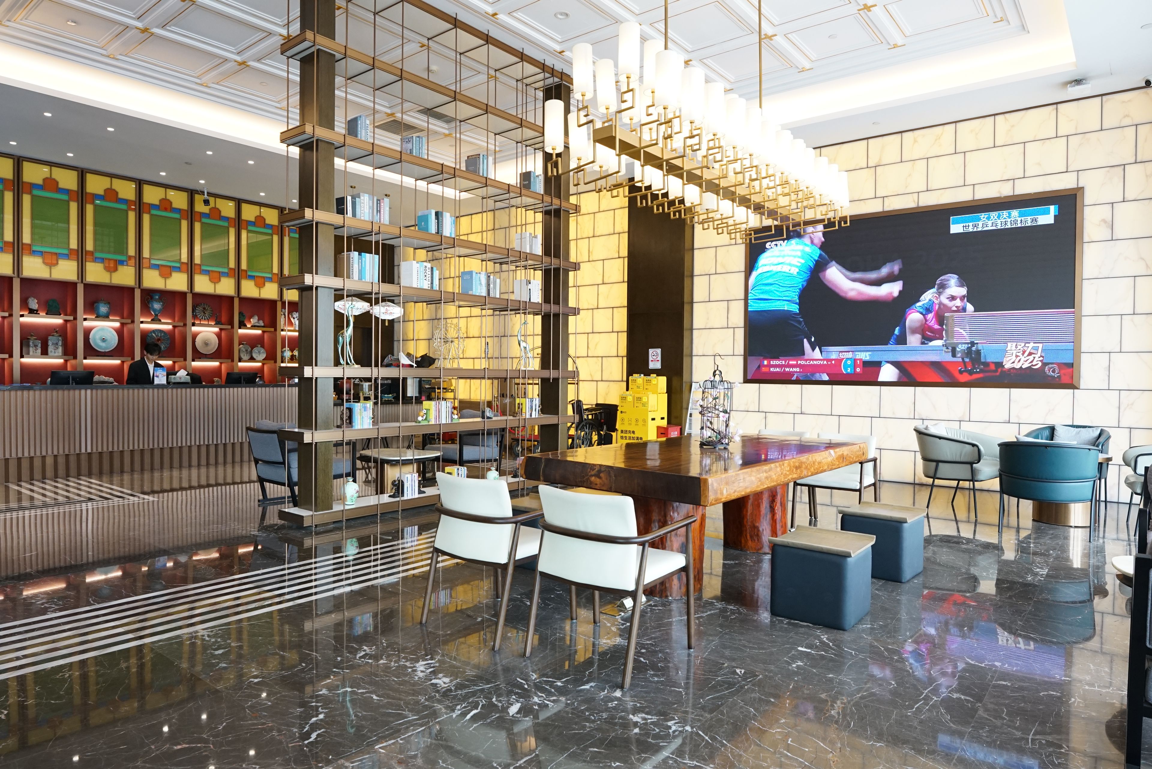Un lobby moderno con zona de bar, asientos, una pantalla grande y una estantería decorativa.