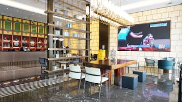 Un lobby moderno con zona de bar, asientos, una pantalla grande y una estantería decorativa.