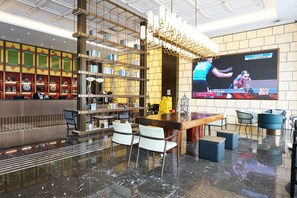 Um lobby moderno com área de bar, assentos, uma grande tela de TV e uma estante decorativa.