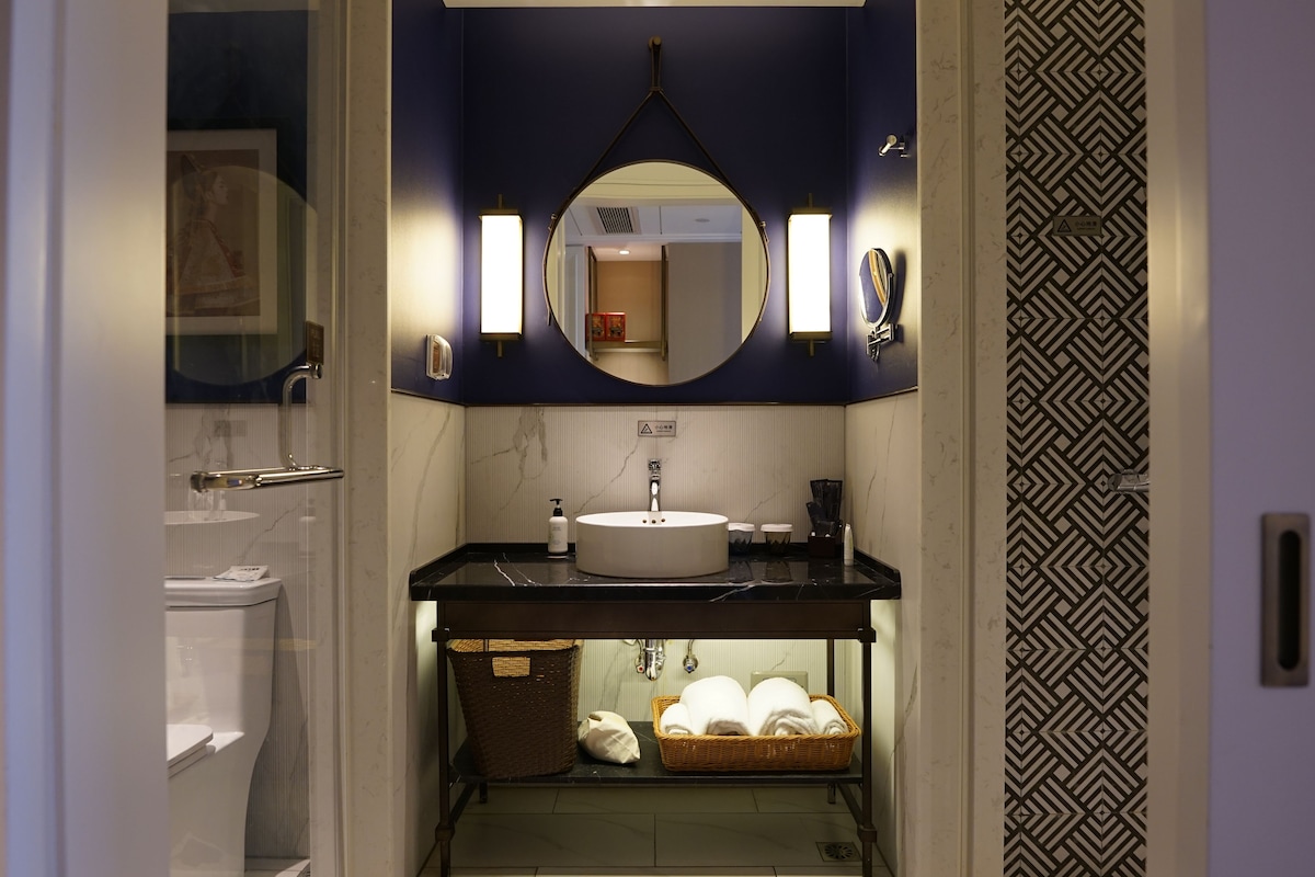 Un baño con un espejo redondo, un lavabo y un perchero para toallas.
