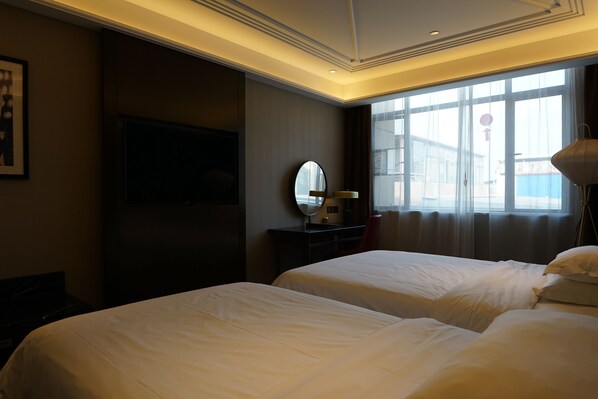 A hotel room with two beds, a flat-screen TV, a mirror, and a window with curtains.