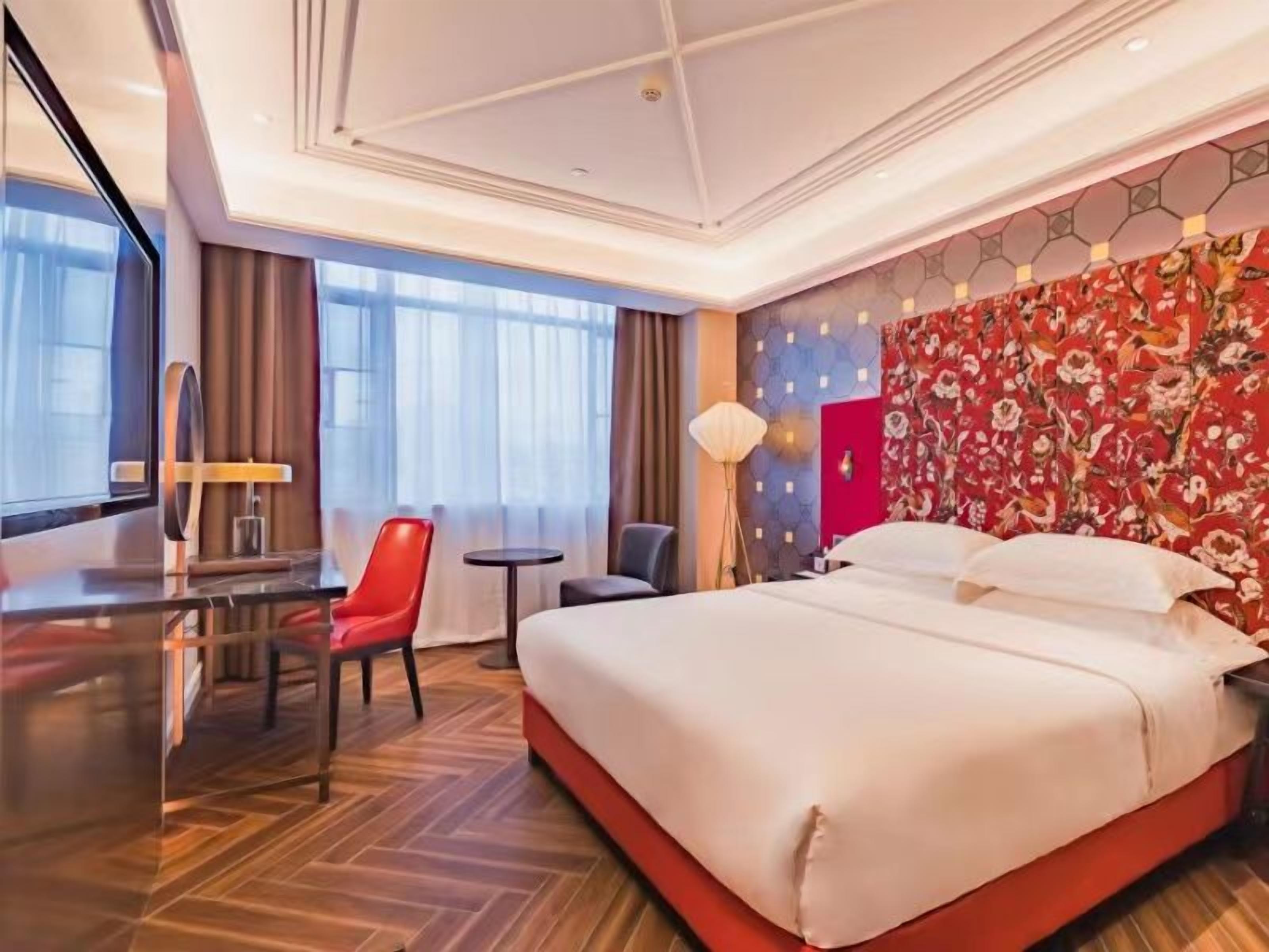A hotel room with a large bed, a desk, a chair, and a small table.