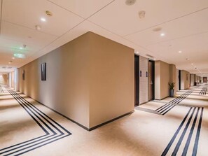 Un couloir d’hôtel avec une colonne centrale, des portes de chaque côté et un tapis à motifs.