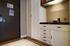 Une chambre d’hôtel avec un plancher en bois, une armoire blanche avec des tiroirs, un comptoir noir et un petit réfrigérateur.