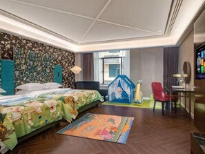 A hotel room with a large bed, a play area, a red chair, and a television.