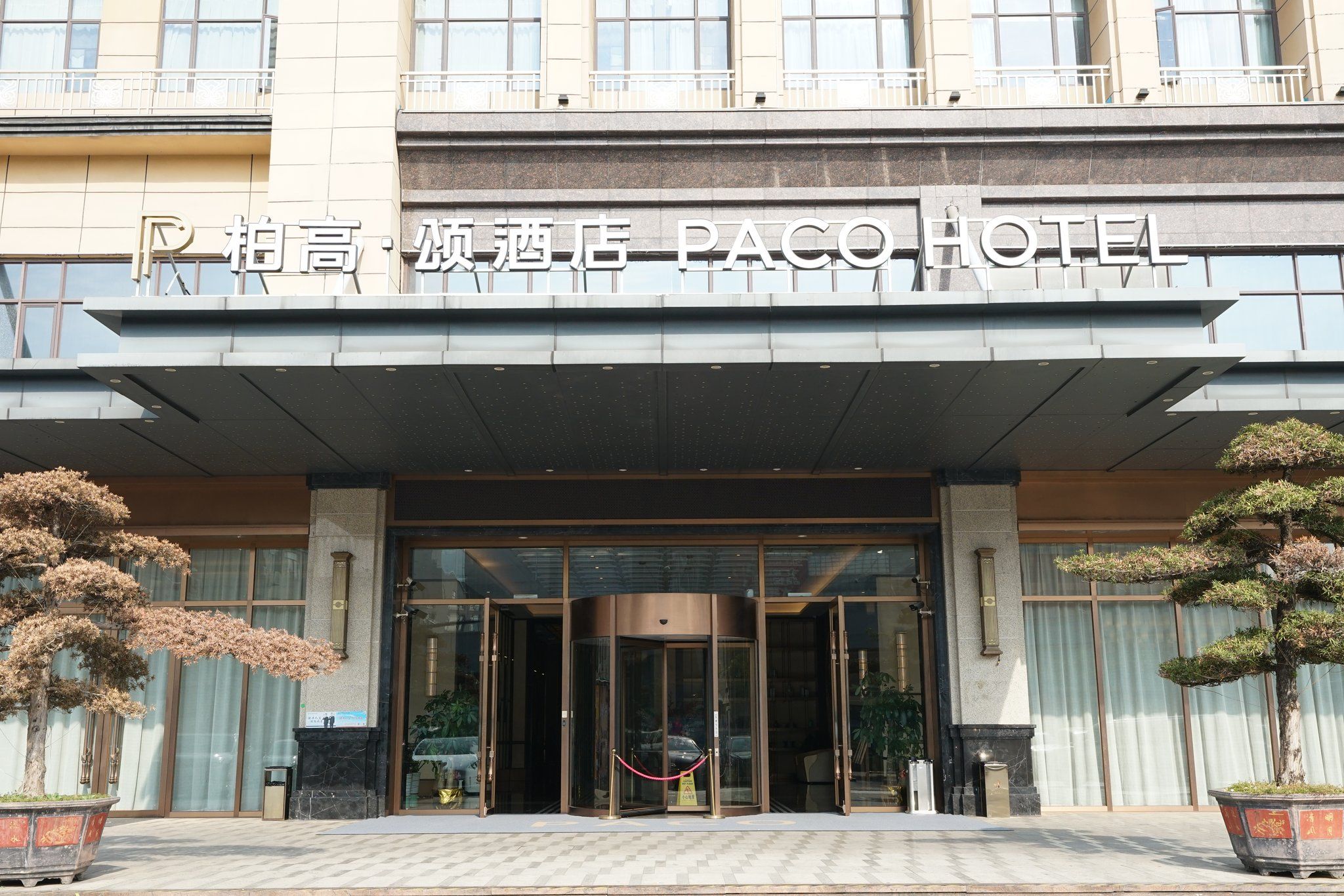 The entrance of a hotel with a modern facade, glass doors, and a sign indicating it's a PACC hotel.