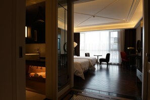 Une chambre d’hôtel comprenant un lit, un bureau, une chaise, une petite table et une salle de bain avec un lavabo et un miroir.
