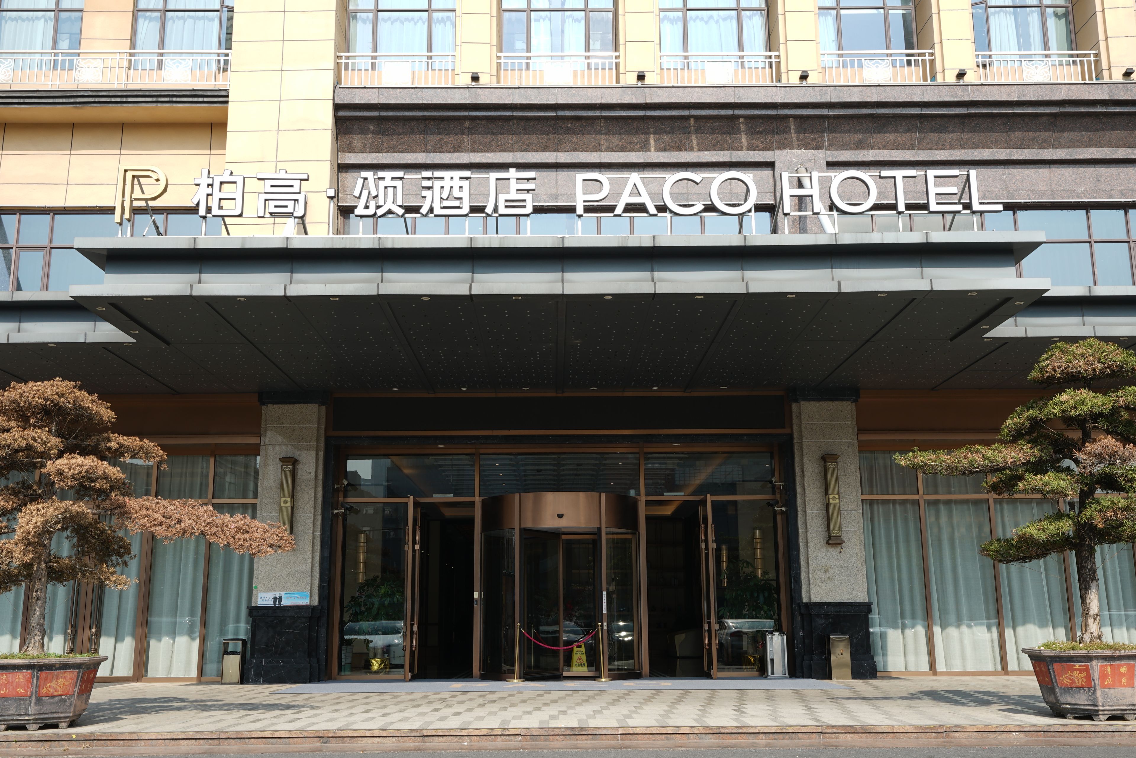 The facade of a hotel with a prominent entrance, a sign indicating it's a Paco Hotel, and traditional Chinese architectural elements.