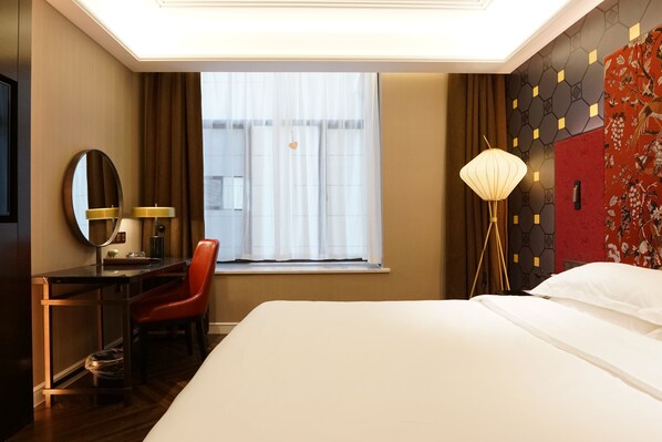 Habitación de hotel con cama, escritorio, silla, lámpara de escritorio, espejo y ventana con cortinas.