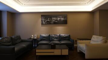 Una sala de estar moderna con un sofá de cuero negro, un sillón blanco y una mesa de centro. Un cuadro de un paisaje urbano está colgado en la pared.
