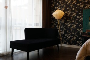 A room with a black sofa, a floor lamp, and a floral wallpaper.