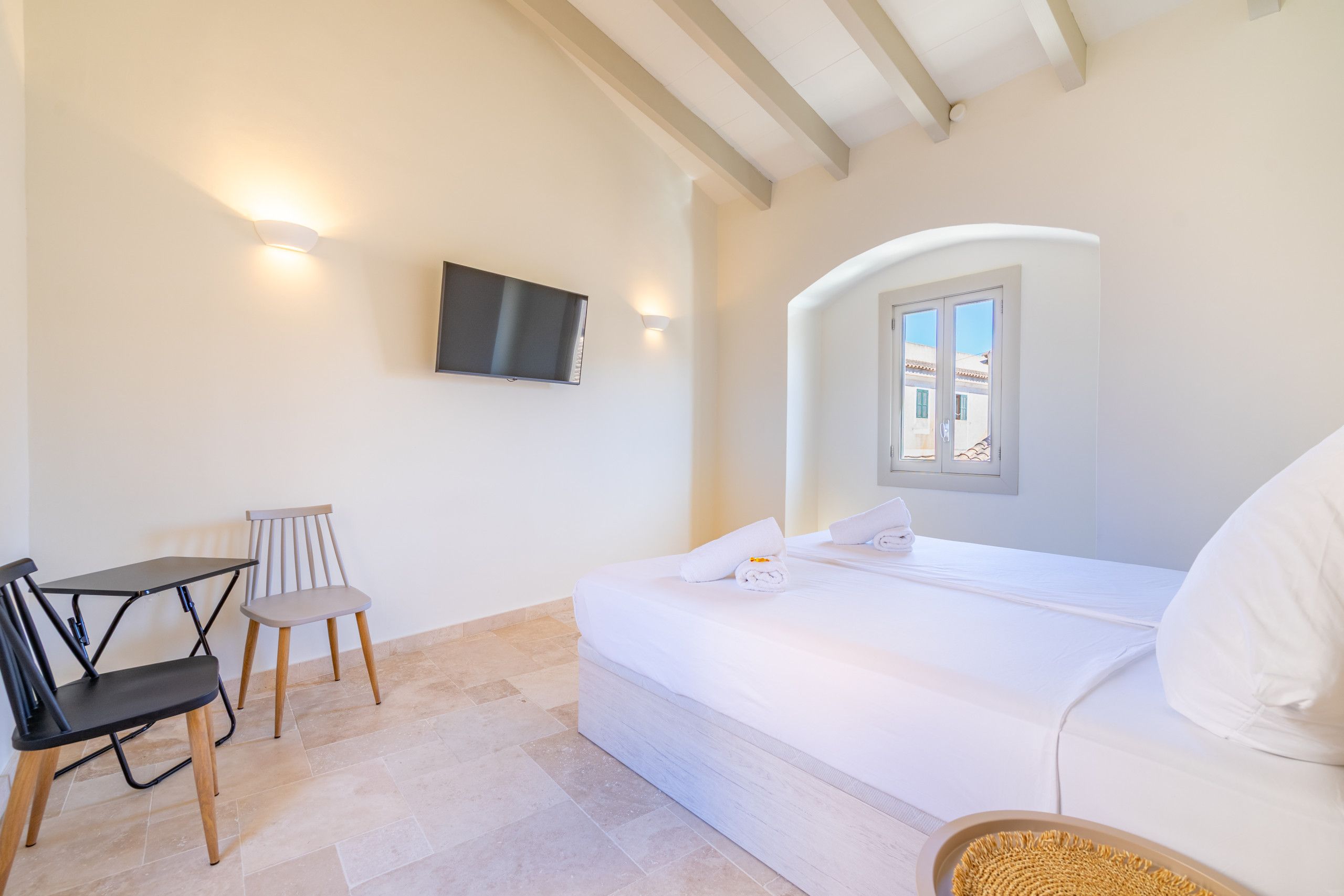 A hotel room with a bed, a desk, a chair, a television, and a window.