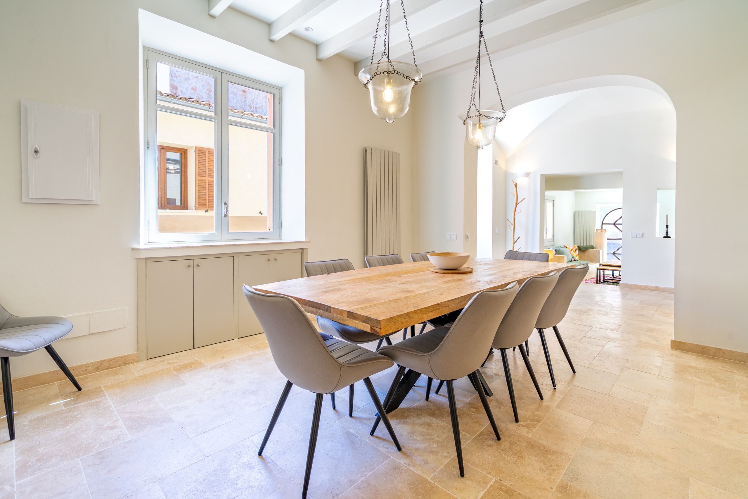 A spacious dining area with a wooden table and modern chairs, large windows, and a view of the outside.
