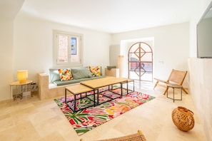 A modern living room with a sofa, a coffee table, a chair, a colorful rug, and a large window. - Ses Rocasses - 8 minutes away from the beach (Santanyi)