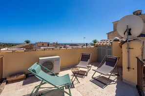 A rooftop terrace with two lounge chairs, an air conditioning unit, and a satellite dish.