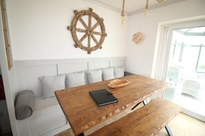 A wooden table with a notebook, a woven wall decoration, and a bench with pillows. - Moorehouse Holiday Let 3-Bed Bungalow (Lancashire)
