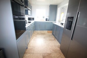 A modern kitchen with grey cabinets, stainless steel appliances, and a tiled floor. - Moorehouse Holiday Let 3-Bed Bungalow (Lancashire)