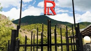Un letrero con las letras 'HOTEL' y 'R' montado sobre un marco metálico negro, con un paisaje montañoso al fondo.