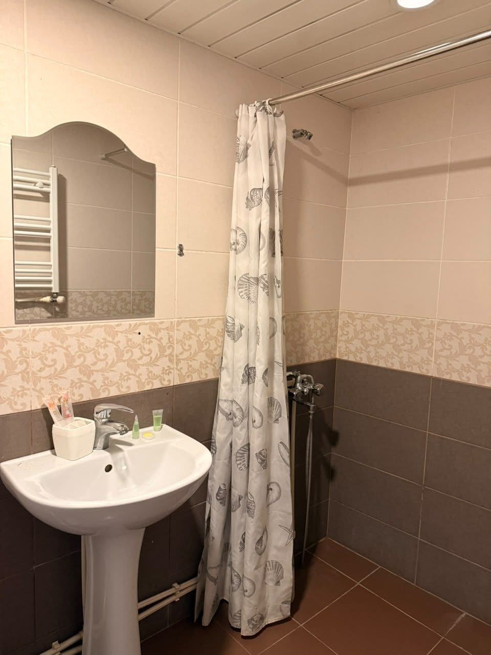 A bathroom with a white pedestal sink, a mirror, a shower with a curtain, and tiled walls.
