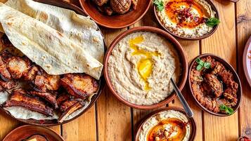 Variedad de platos, incluyendo carnes a la parrilla, hummus y ensaladas, que sugieren una amplia selección de comidas.