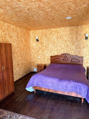 A bedroom with a wooden headboard, a bed with a purple bedspread, a wooden wardrobe, and a small bedside table. - Restland Hotel  (Dilijan)
