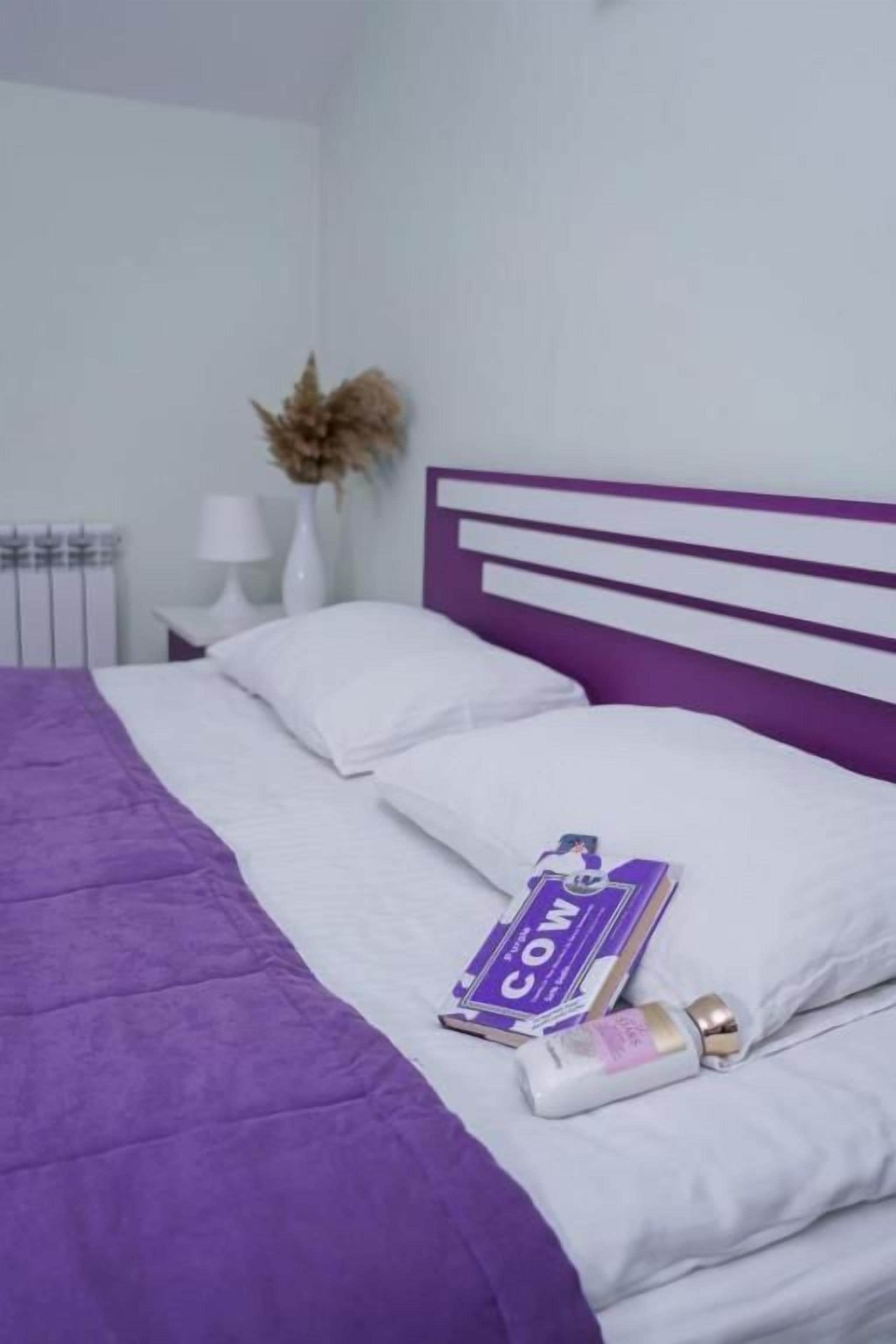 A bed with a purple headboard, white bedding, and a book titled 'Cow' on the pillow.