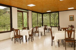 Un comedor con mesas y sillas, ventanas amplias y vista a zonas verdes exteriores.